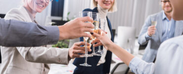 A group of individuals in office apparel gather in a circle, toasting glasses of champagne in celebration.