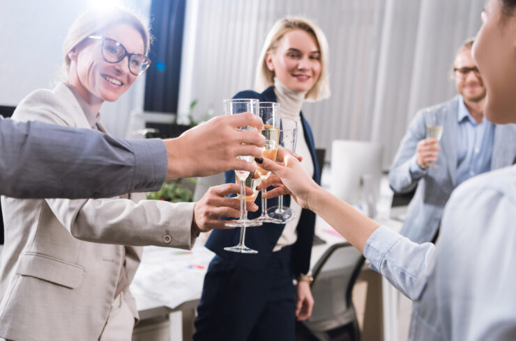 A group of individuals in office apparel gather in a circle, toasting glasses of champagne in celebration.